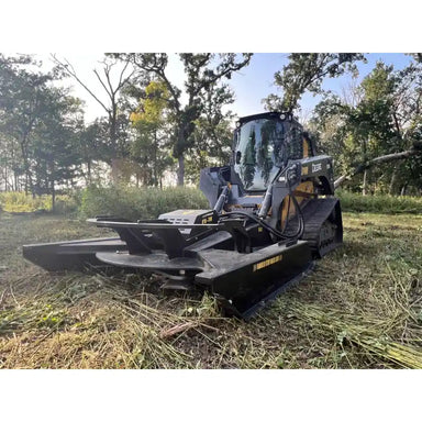 Skid steer brush cutter attachment with 1” pan, four blades, and open front design in outdoor wooded setting