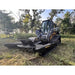 Skid steer brush cutter attachment with 1” pan, four blades, and open front design in outdoor wooded setting