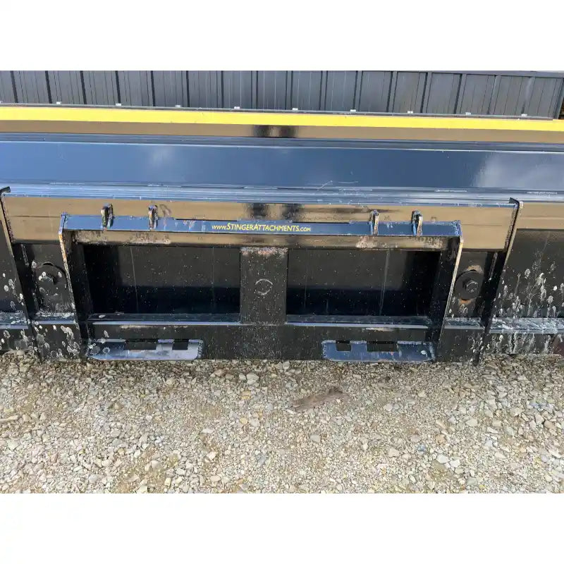 Close-up of black metal skid steer snow pusher attachment mounting plate on gravel ground outdoors