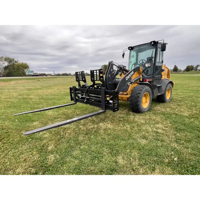 Yellow Deere skid steer with attached black pallet forks featuring solid backrest, parked on grassy field under cloudy sky