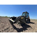 Low-angle front-right view of tracked skid steer with rock bucket reel attachment on dry tilled field under clear sky
