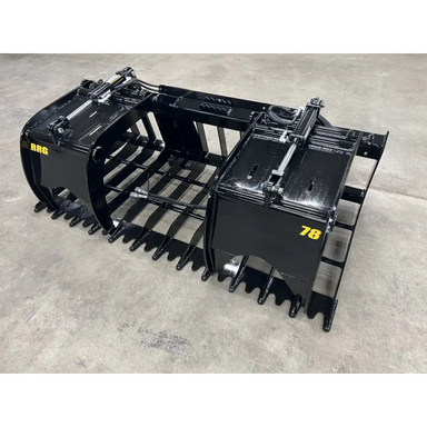 Black steel root and rock grapple skid steer attachment with wide spaced tines and dual hydraulic cylinders on concrete floor
