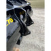 Close-up of black steel bucket attachment showing side mount brackets and part of curved bucket edge on gravel ground