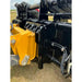 Close-up of yellow loader arm attached to black steel clam-style grapple with visible hydraulic lines on grass field
