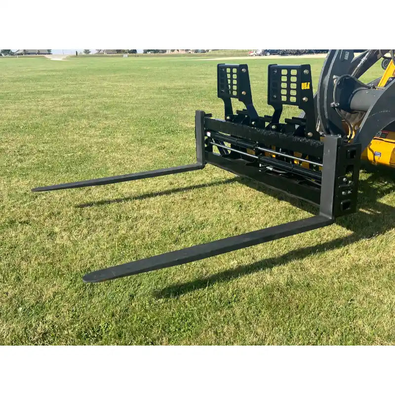 Black steel skid steer pallet fork attachment with two extended tines and perforated vertical backrest on grass field outdoors