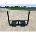 Black steel skid steer attachment with two vertical arms and flat lifting plates on gravel surface viewed from front angle