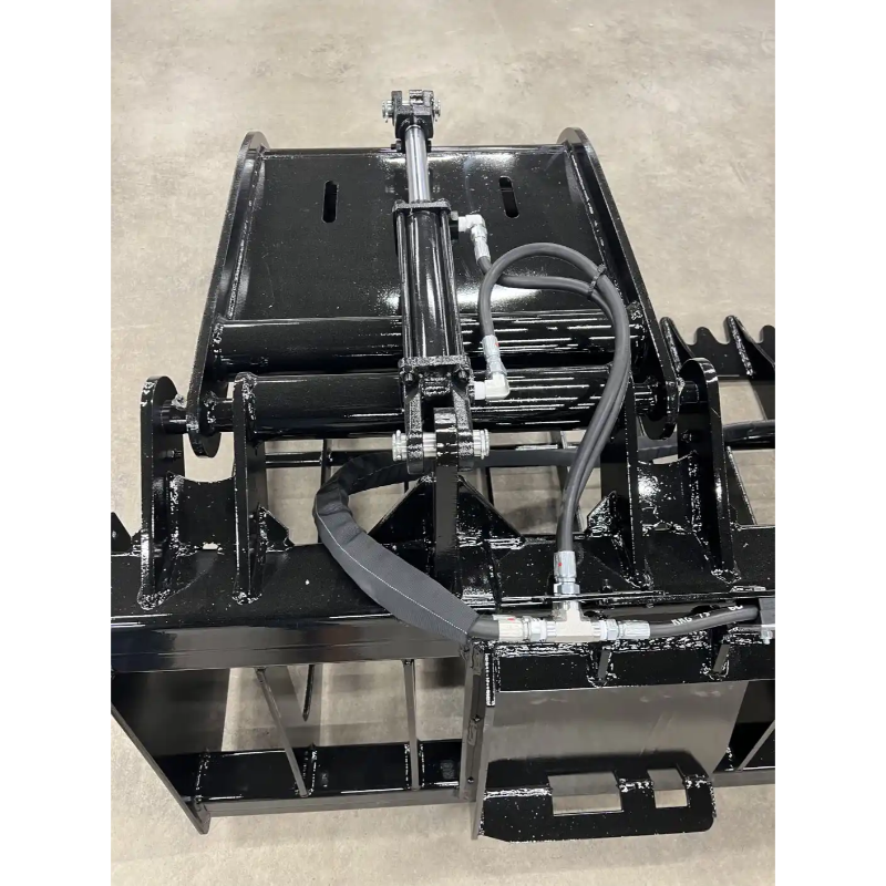 Black skid steer grapple attachment with hydraulic cylinder, reinforced frame, and steel mounting bracket on concrete floor