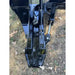 Close-up of black steel tree puller attachment with hydraulic cylinder and mounting bracket on grass with leaves