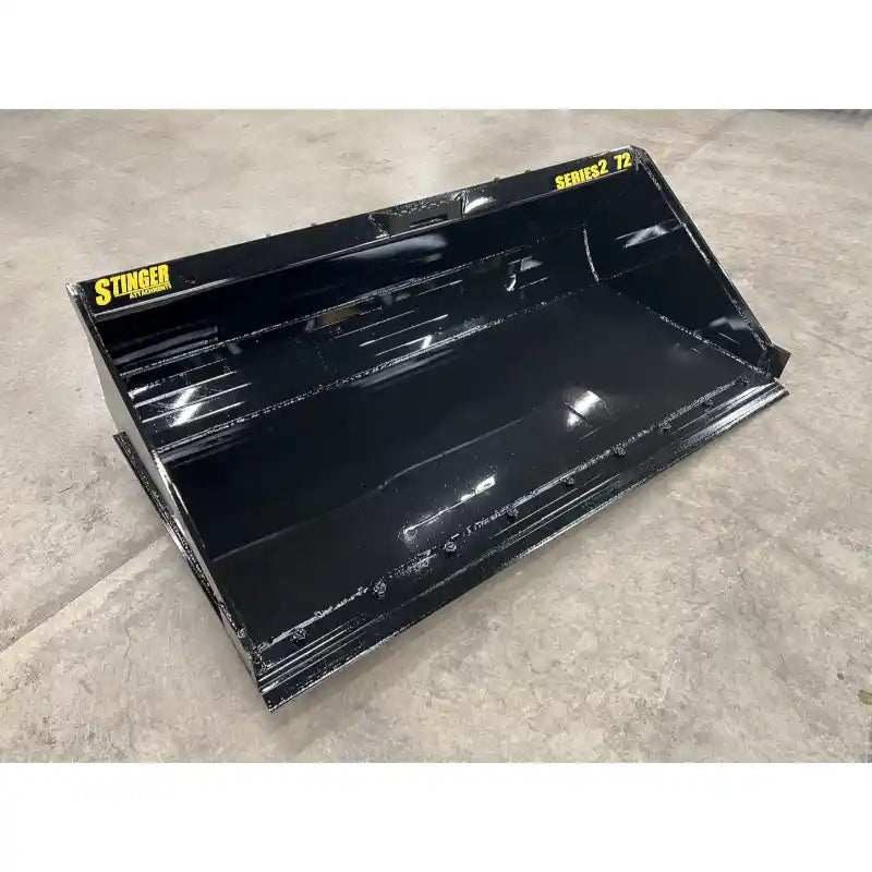 Flat black steel skid steer material bucket with reinforced welds, smooth interior, and yellow Stinger Series 2 72 labels on concrete floor
