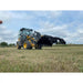 Yellow John Deere wheel loader operating with large black steel clam-style grapple attachment over dry grassy field under cloudy sky