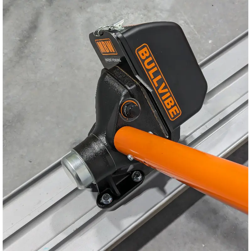 Close-up of black mechanical float attachment with orange handle mounted on aluminum screed rail on concrete floor