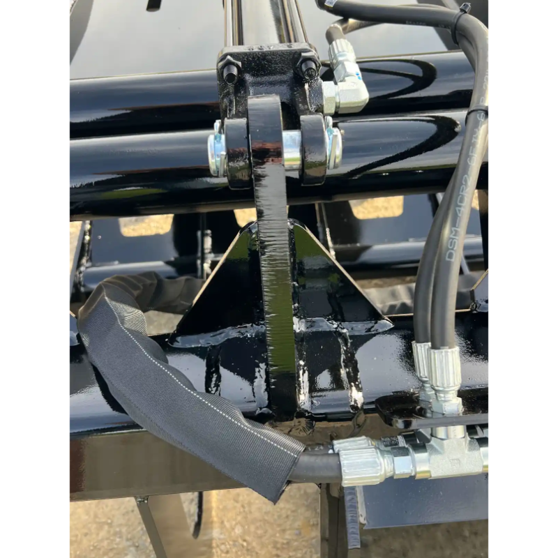 Close-up of black painted steel hinge and hydraulic hose connections on skid steer grapple attachment