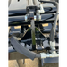 Close-up of black steel skid steer root grapple hinge, hydraulic hose fittings, and mounting bracket on gravel surface