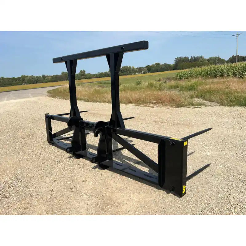 Black steel skid steer bale spear attachment with vertical support arms and four pointed tines on gravel road outdoors