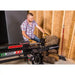 Operator positioning large log on Swisher 22-Ton Timber Brute Eco Split electric log splitter, gallery position 1 indoors
