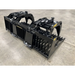 Black painted steel skid steer rock grapple attachment featuring hydraulic cylinders and serrated tines on concrete floor