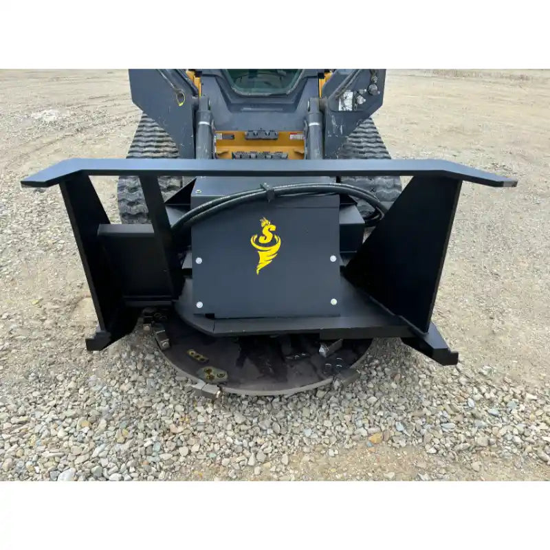 Black steel skid steer attachment with hydraulic hoses and yellow logo mounted on compact track loader on gravel surface