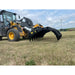 Yellow John Deere loader fitted with black steel grapple attachment lowered over dry grass field under cloudy sky