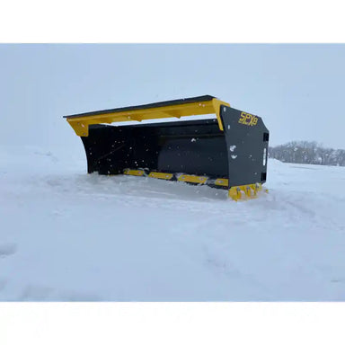 Black and yellow skid steer snow pusher attachment tilted back resting on snow-covered ground outdoors