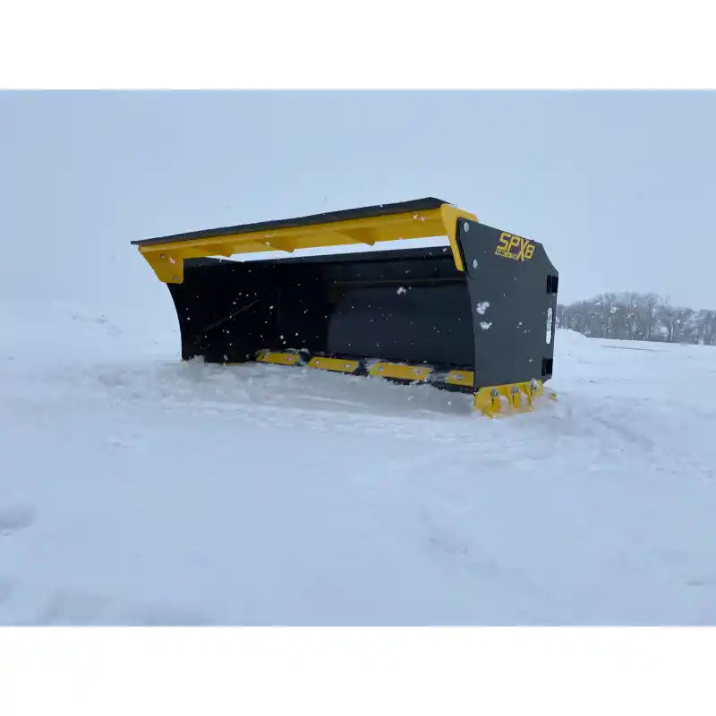 Black and yellow skid steer snow pusher attachment tilted back resting on snow-covered ground outdoors