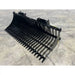 Black metal rock bucket attachment with curved tines and mounting brackets on concrete floor surface