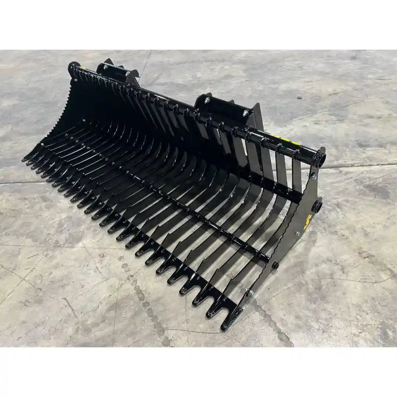 Black metal rock bucket attachment with curved tines and mounting brackets on concrete floor surface
