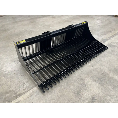 Wide black skid steer rock bucket attachment with evenly spaced tines and reinforced mounting brackets on concrete floor