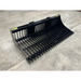 Wide black skid steer rock bucket attachment with evenly spaced tines and reinforced mounting brackets on concrete floor