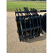 Black steel clam grapple attachment with multiple curved tines and a reinforced frame on gravel surface outdoors