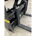 Black steel skid steer pallet fork attachment with reinforced crossbars and two horizontal fork tines on concrete floor