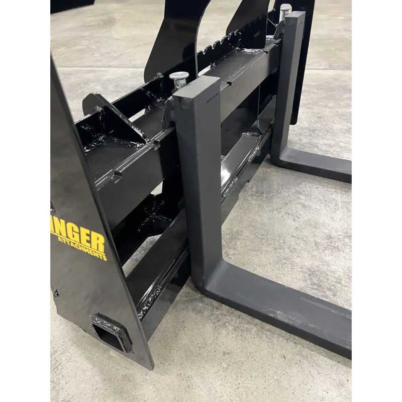 Black steel skid steer pallet fork attachment with reinforced crossbars and two horizontal fork tines on concrete floor