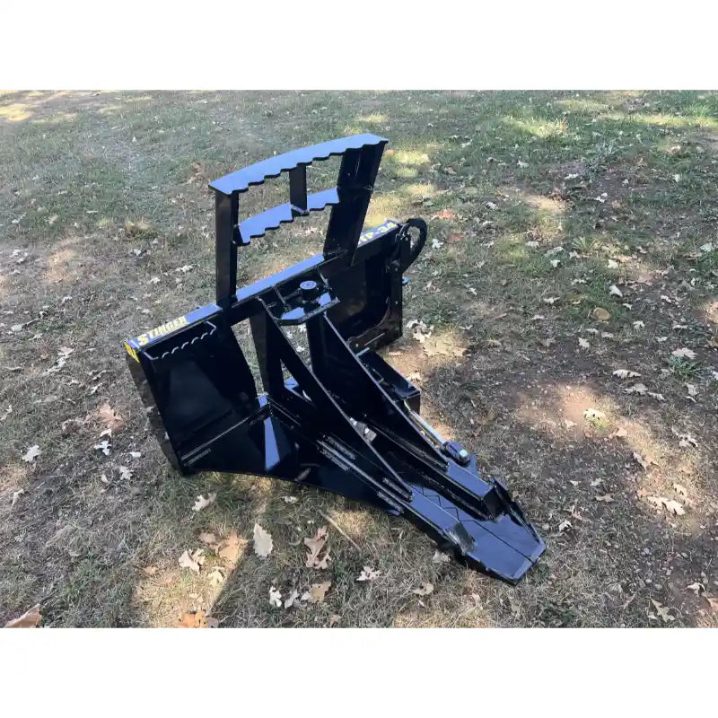 Black steel tractor tree puller attachment with serrated gripping plate and angled frame on grassy ground with scattered leaves