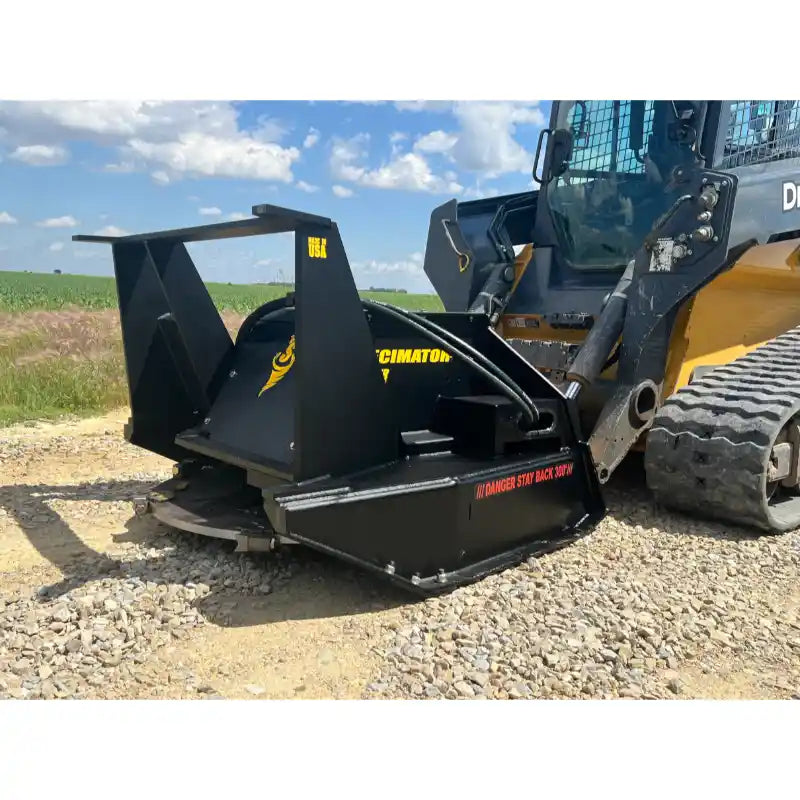 Black steel disc mulcher attachment connected to tracked skid steer loader on gravel and grass field background