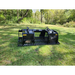 Black skid steer grapple attachment with spaced parallel tines, hydraulic cylinders, and solid side panels on grass surface