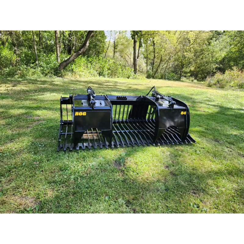 Black skid steer grapple attachment with spaced parallel tines, hydraulic cylinders, and solid side panels on grass surface