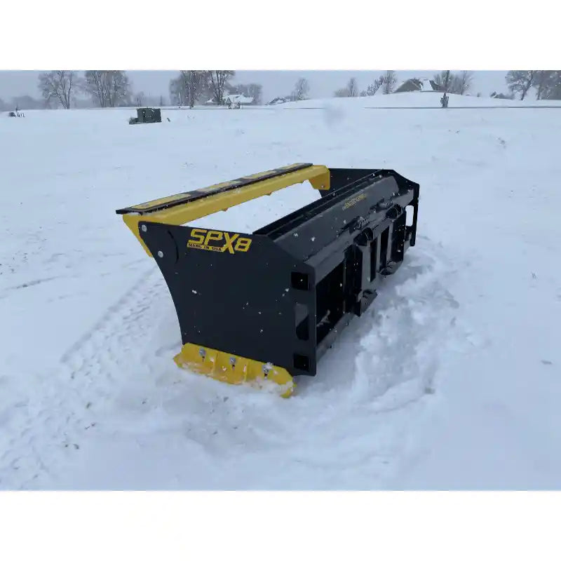 Rear left angle of black and yellow skid steer snow pusher attachment sitting on snow-covered ground outdoors