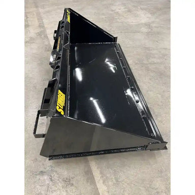 Black steel skid steer material bucket with smooth interior and yellow Stinger Series 2 labels on concrete floor