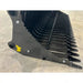 Close-up of black metal rock bucket attachment with curved spaced tines and reinforced side plates on concrete floor