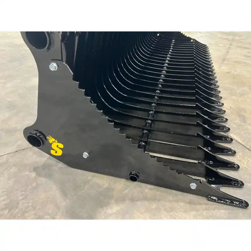 Close-up of black metal rock bucket attachment with curved spaced tines and reinforced side plates on concrete floor