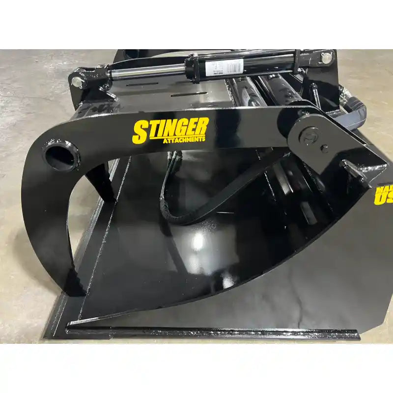 Black metal skid steer grapple bucket attachment with hydraulic cylinder and curved clamp arm on concrete floor