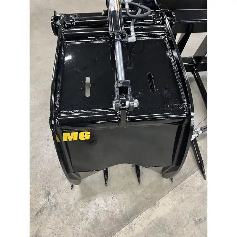 Black metal manure grapple attachment with hydraulic cylinder, rounded tines, and solid frame on concrete floor indoors