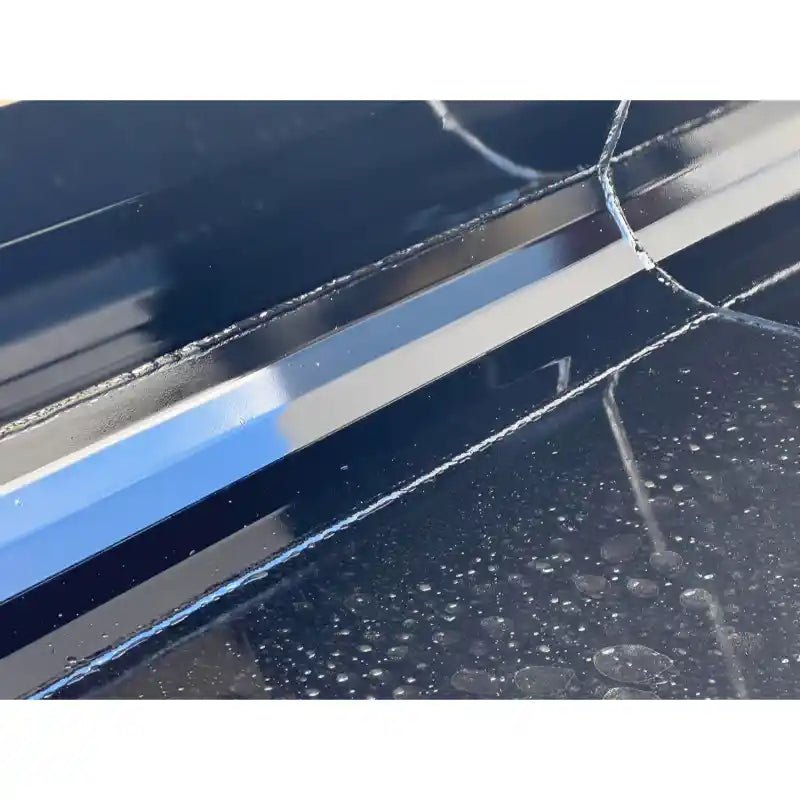 Close-up of welded black steel snow bucket edge with smooth paint finish and water droplets on surface