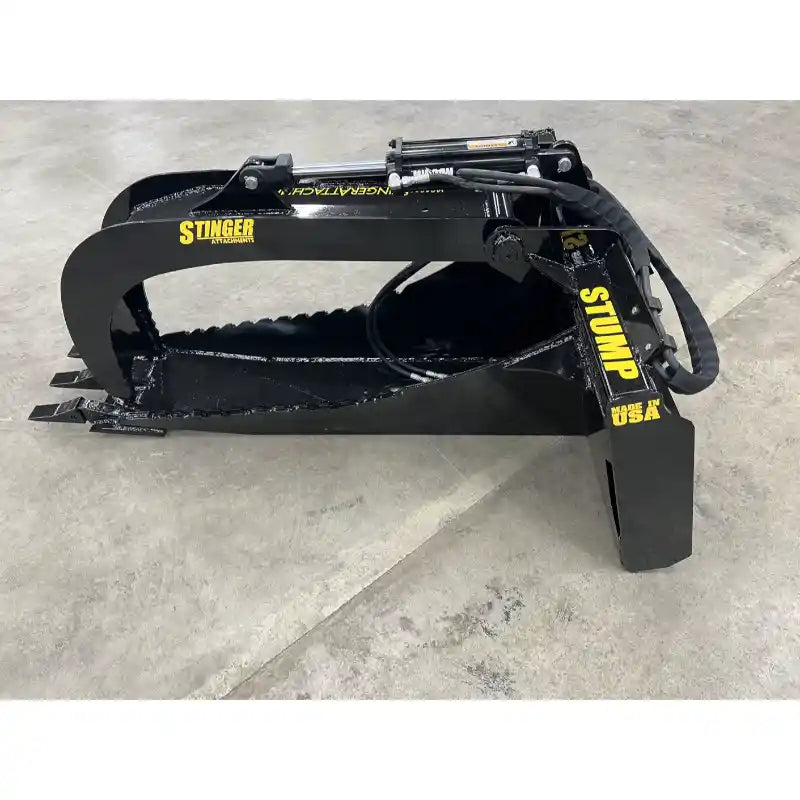 Black steel skid steer grapple attachment with serrated edges and hydraulic cylinder on concrete floor