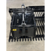 Close-up of black steel rock grapple attachment with hydraulic cylinder and curved tines on concrete floor