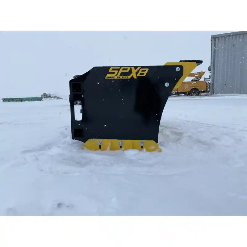 Side view of black and yellow skid steer snow pusher attachment standing on snow-covered ground outdoors