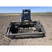 Front view of JCB skid steer with rock reel attachment lifting rocks from dry field soil under clear sky