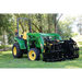 Green compact tractor equipped with large black steel grapple attachment on grass under trees outdoors