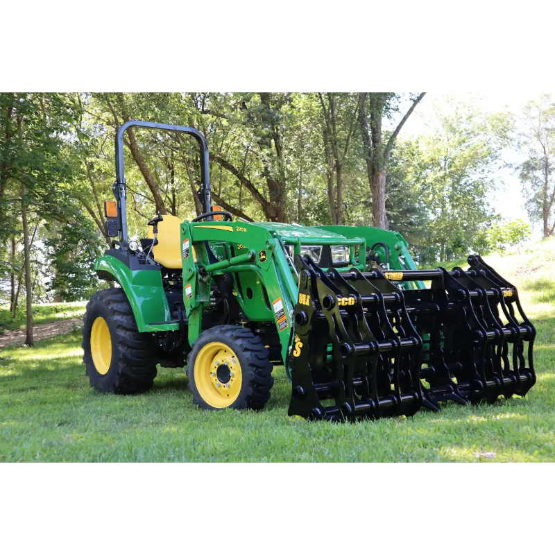 Green compact tractor equipped with large black steel grapple attachment on grass under trees outdoors