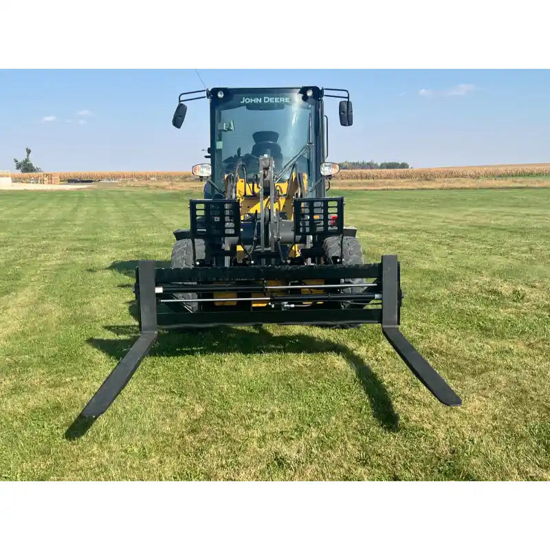 Yellow John Deere loader equipped with black skid steer pallet fork attachment on a grassy field