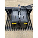 Black steel skid steer grapple attachment with wide flat curved tines, hydraulic cylinder, and hoses on gravel surface outdoors